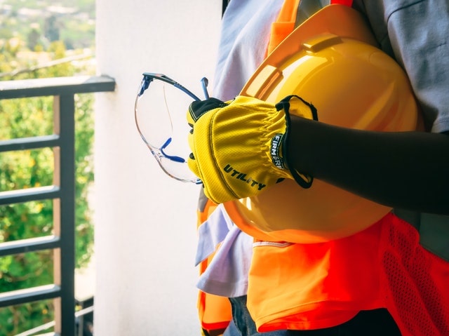 A roofer with a hardhat and vest on standing on a balcony.